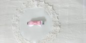 Fermaglietto da bambina a forma di molletta decorato con fiocchetto di raso bianco e con un'altro fiocchetto rosa sovrapposto.