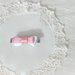 Fermaglietto da bambina a forma di molletta decorato con fiocchetto di raso bianco e con un'altro fiocchetto rosa sovrapposto.