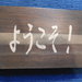 pannello inciso con scritta "benvenuti" in giapponese in legno di rovere