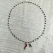 Collana girocollo stile rosario con filo di colore argento, cristalli neri e ciondoli con lettera e cornetto portafortuna rosso.