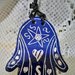 6° ciondolo  esoterico di ceramica, manufatto a forma di mano di Fatima con sella di Davide sul dorso e cuori fiori e gnci sulle dita , motivo graffito bianco su fondo blu