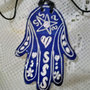 6° ciondolo  esoterico di ceramica, manufatto a forma di mano di Fatima con sella di Davide sul dorso e cuori fiori e gnci sulle dita , motivo graffito bianco su fondo blu