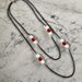 Collana medio lunga con catenella nera in alluminio e inserti di perle di pietra dura bianche e rosse
