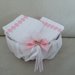 Elegante cestino foderato con raso bianco decorato con delicato fiocco rosa contenente una coppia di lavette decorate con pizzo macramè