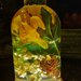 Lampada a forma di bottiglia con gerbera gialla e pigne