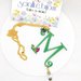 Collana lunga con catenina dorata e lettera M verde pendente, decorata con perle di vetro