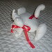 Pupazzo gatto in panno imbottito color bianco con fiocchi rossi. Ideale per abbellire i letti dei bambini