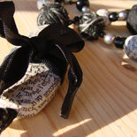 Collana con perline fatte a mano con carta di quotidiani e con fili di lana intrecciati intervallate da perline in plastica nere e grigie.