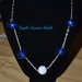 collana con decori realizzati con pepite di plastica blu e perle bianche, con perla bianca centrale