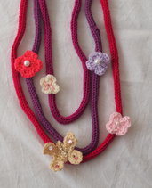 COLLANA in maglia di lana(tricotin) 3 fili.Applicazione di 4 fiori uncinetto e 1 farfalla.Strass,perline,perle.Toni del viola.Diversi colori