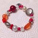 Braccialetto con perle e perline elastico nelle tonalità del rosso, bianco e argento con ciondolino a fiore, fatto a mano 
