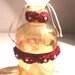 Bottiglietta in vetro fumè color ambra decorata a mano con roselline rosso scuo assemblate e cucite su un nastro in tulle con una piccola perla al centro di ognuna