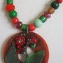 Collana perline toni rosso-verde e pendente in legno di cocco con applicazioni di vetro e strass