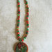 Collana perline toni rosso-verde e pendente in legno di cocco con applicazioni di vetro e strass