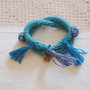 BRACCIALE Turchese e blu mèlange in maglia di lana tubolare.Due giri intrecciati con applicate 2roselline mèlange e 3nappine.Ciondolo :farfalla.(Della parure 4 pz.in vendita)