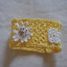 Bracciale di cotone giallo,in pizzo all'uncinetto.Applicazione di 3 fiori bianchi.Fiore centrale:stella alpina con perle dorate. Chiusura: bottoncini.