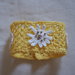 Bracciale di cotone giallo,in pizzo all'uncinetto.Applicazione di 3 fiori bianchi.Fiore centrale:stella alpina con perle dorate. Chiusura: bottoncini.