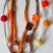 Collana in maglia tubolare.2 fili scalari(lana-seta-cotone)4 fiori a crochet(arancio-marrone).Bottoni a cuore (legno)Filo di palline in feltro in tinta