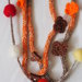 Collana in maglia tubolare.2 fili scalari(lana-seta-cotone)4 fiori a crochet(arancio-marrone).Bottoni a cuore (legno)Filo di palline in feltro in tinta