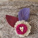 SPILLA in lana e feltro.Due fiori sovrapposti lavorati a telaio,foglie in feltro ricamate.Bottone a cuore in legno.Fuchsia,ciclamino e lilla.